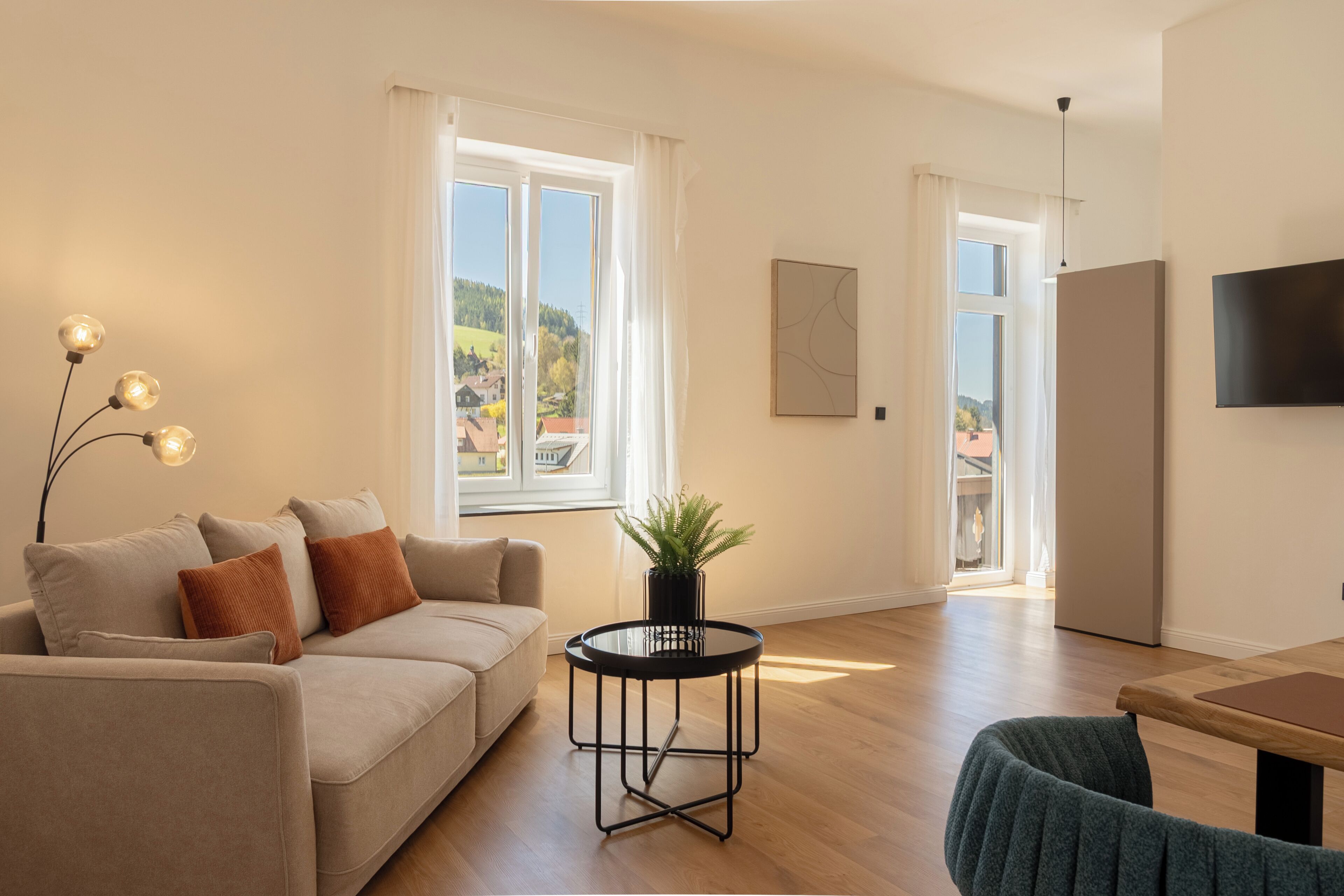 A modern living room with a sofa, a round table, a potted plant, and a TV mounted on the wall.