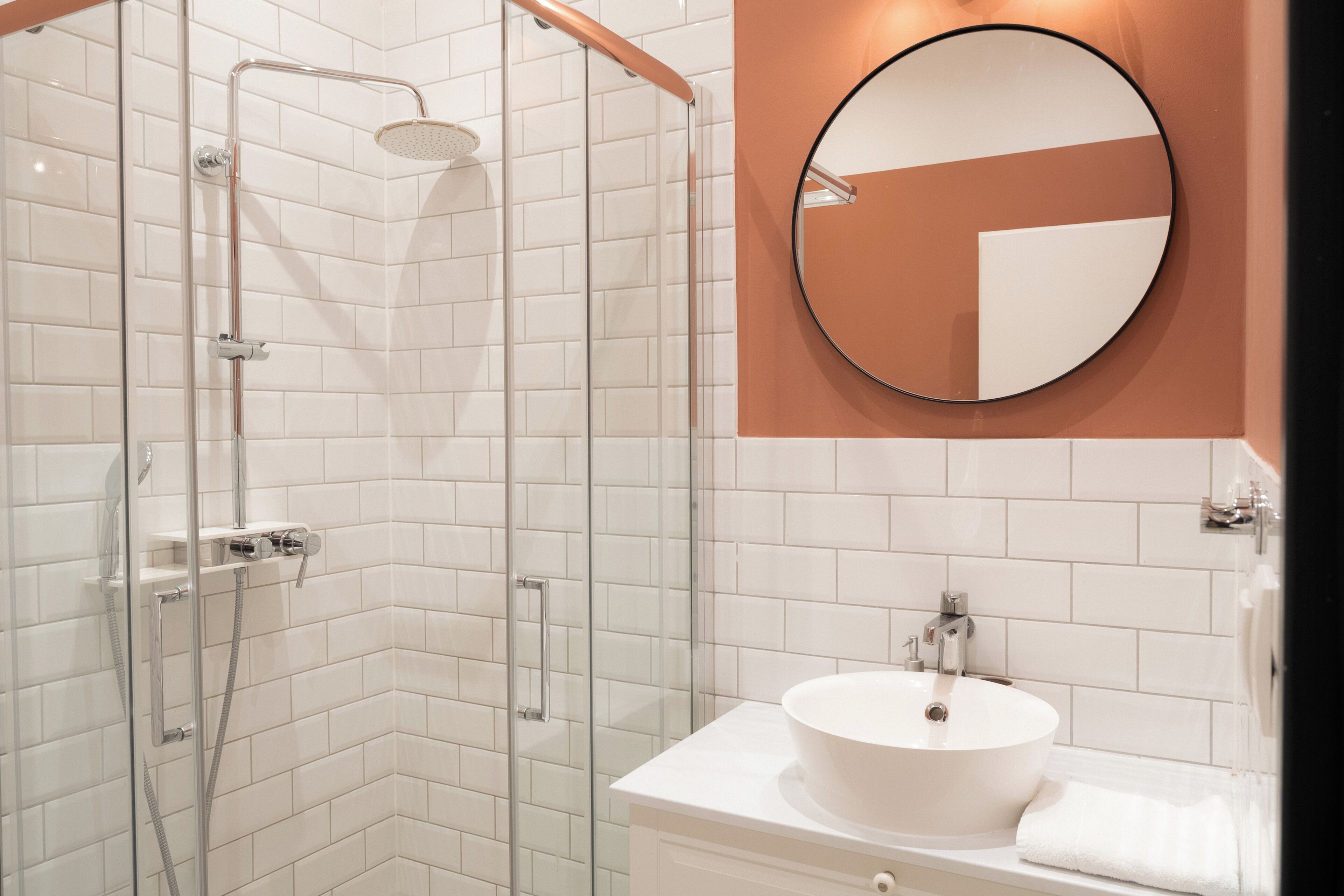A bathroom with a glass-enclosed shower, a white sink, and a round mirror on the wall.