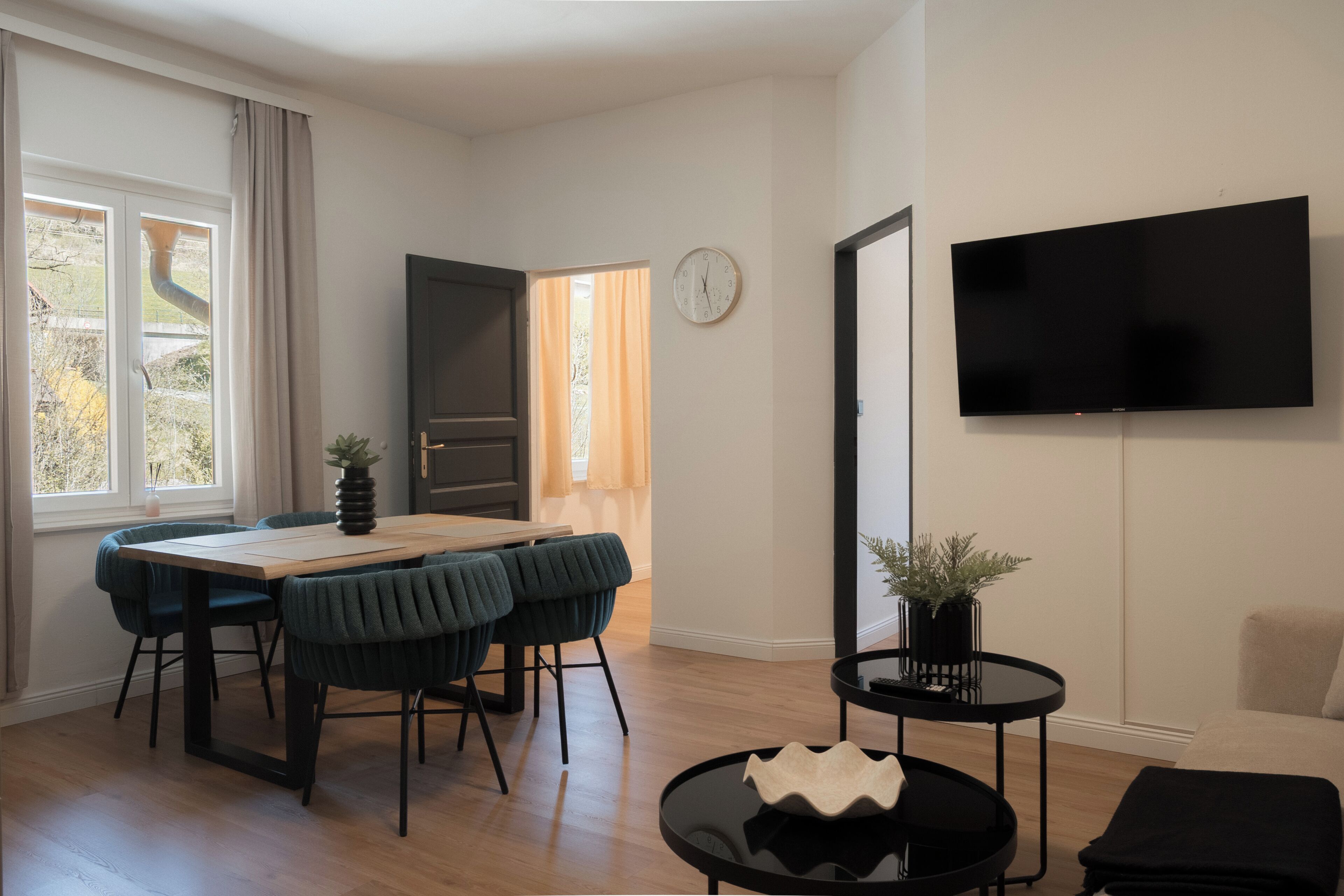 Una sala de estar moderna con comedor, un televisor de pantalla plana montado en la pared y un ventanal con cortinas.