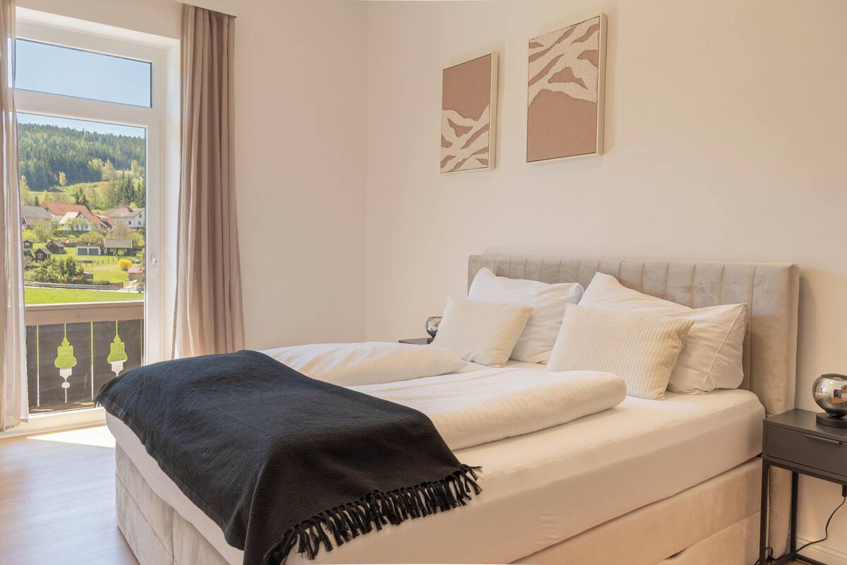 A bedroom with a bed, a nightstand, and a view of a balcony.