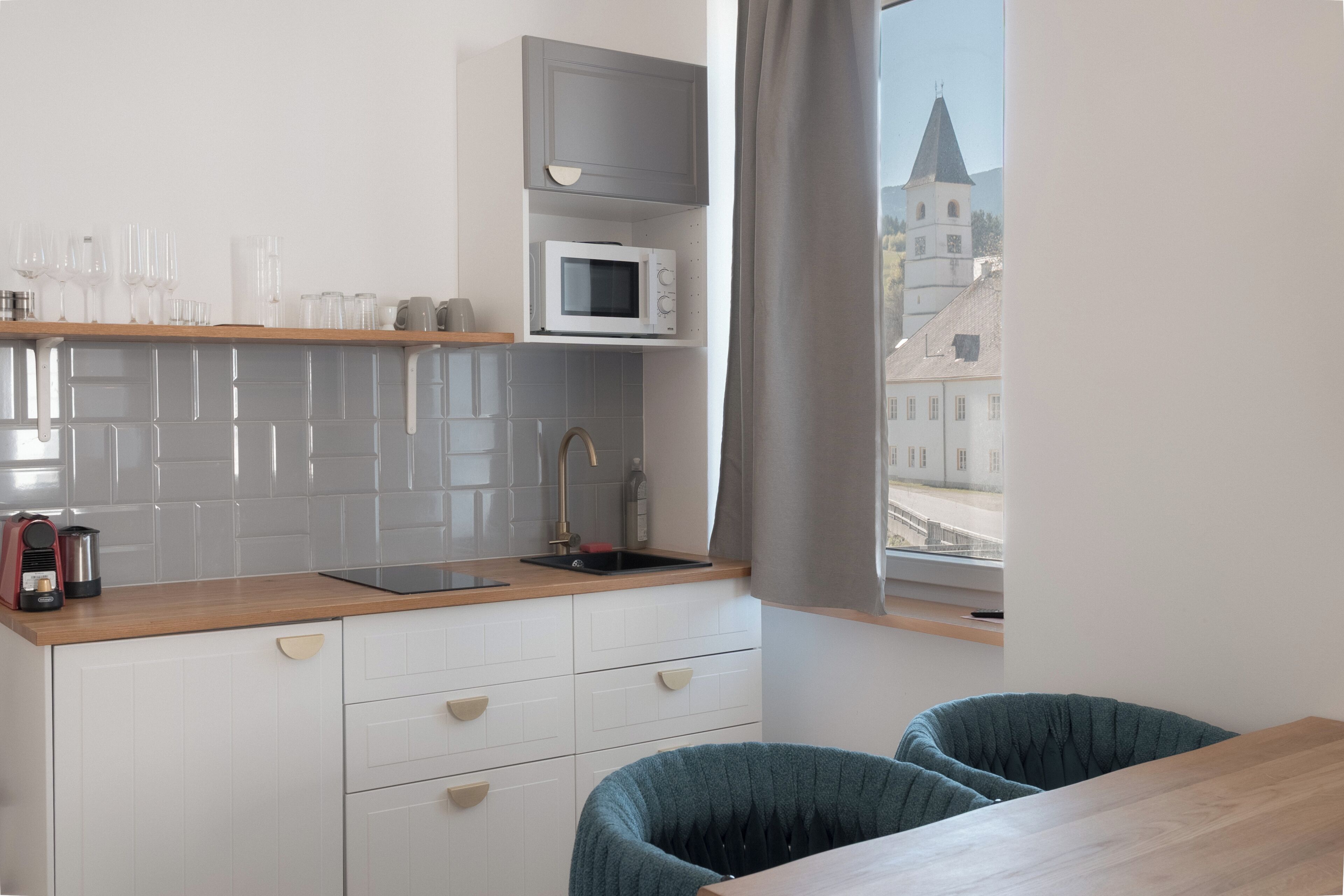 A compact kitchen with a microwave, a sink, and a window overlooking a cityscape.