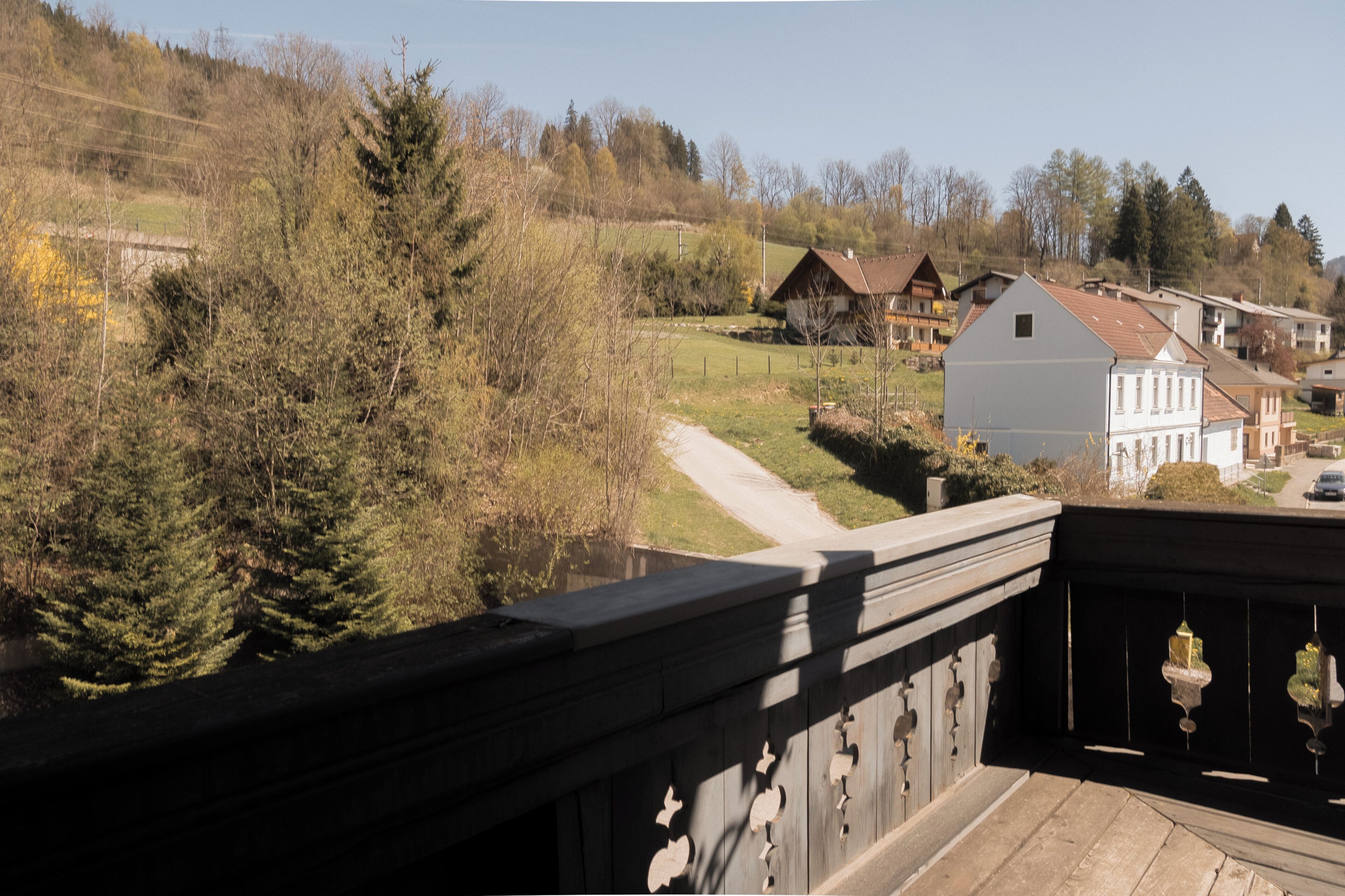 A view from a balcony overlooking a rural landscape with houses, trees, and a clear sky.