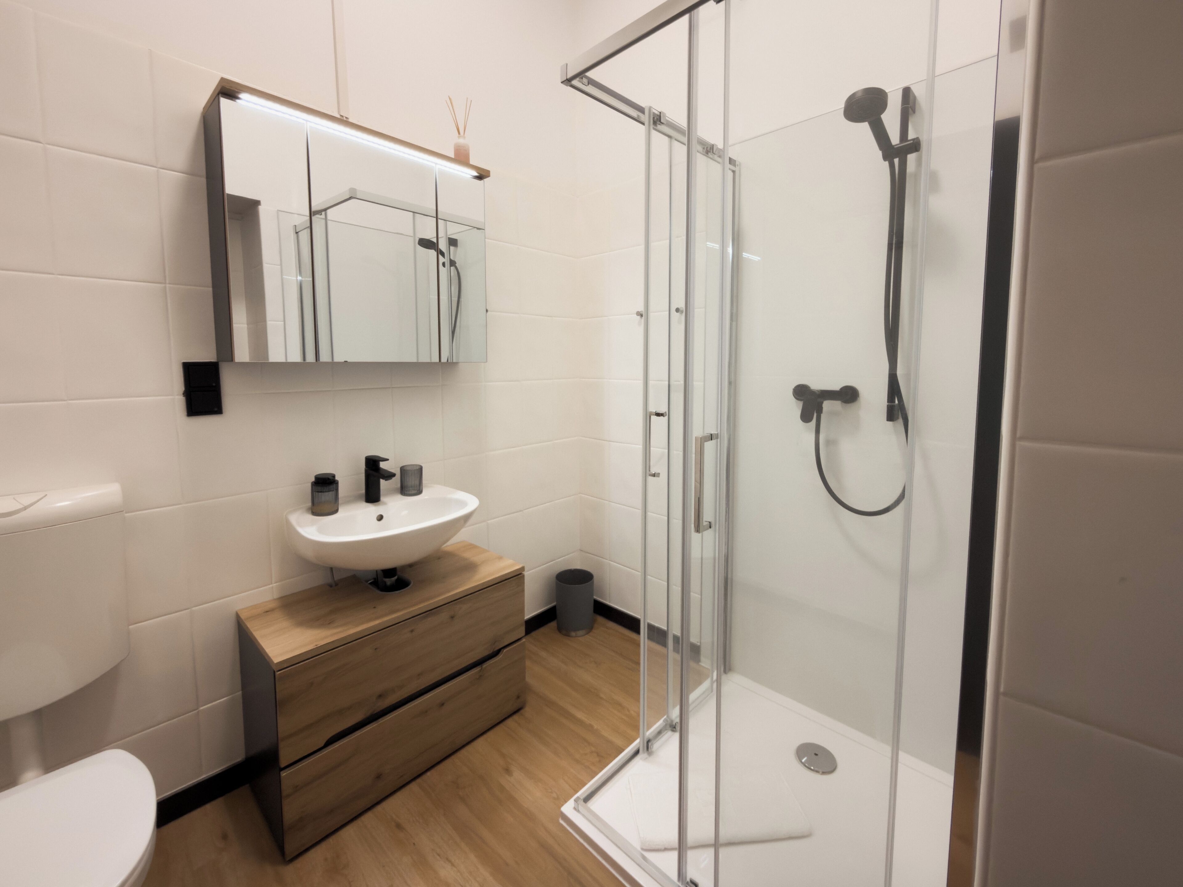 Ein modernes Badezimmer mit Duschkabine aus Glas, einem weißen Waschbecken und einem Holz-Waschtisch.