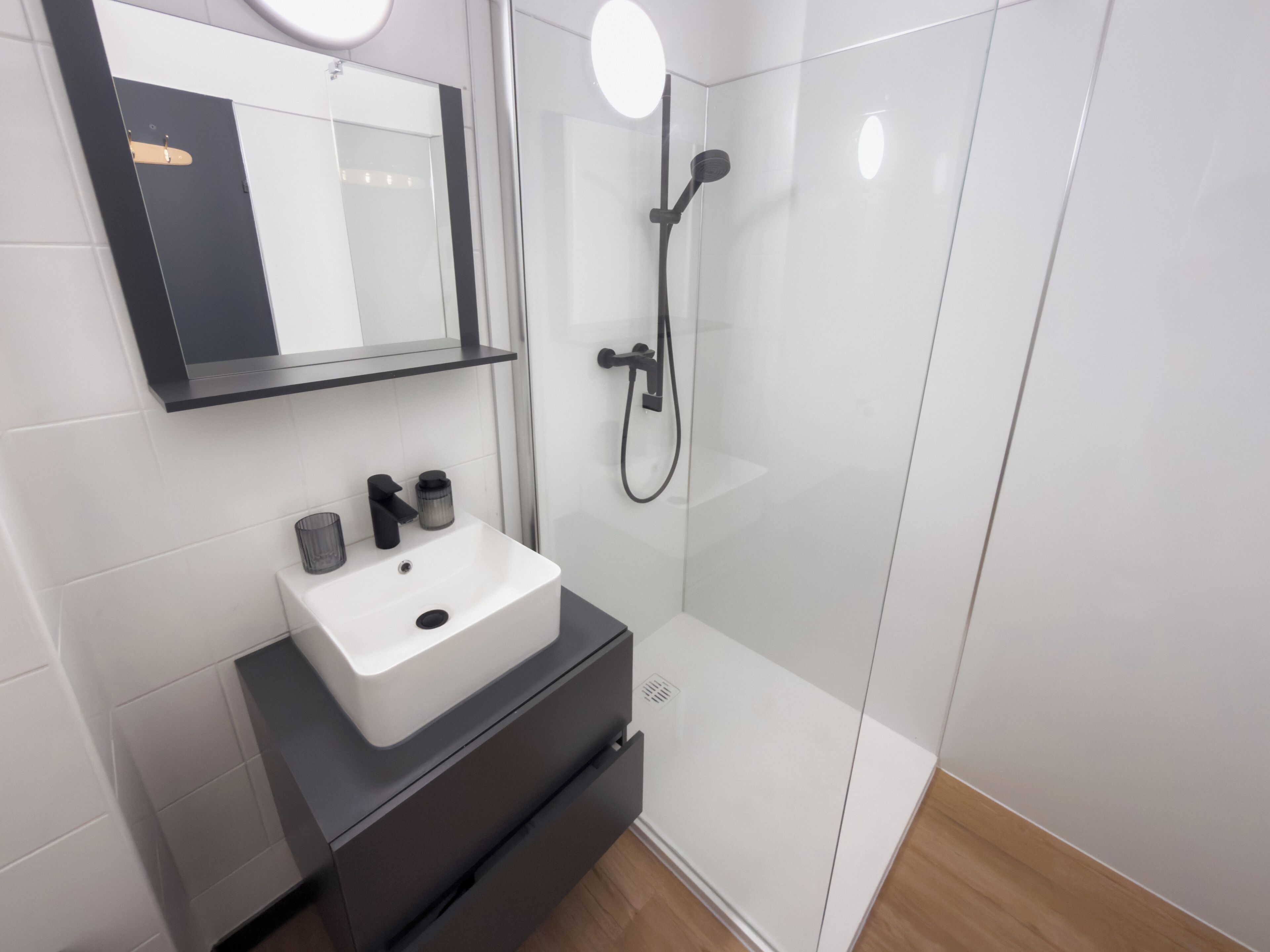 A modern bathroom with a white sink, black vanity, and a glass shower enclosure.