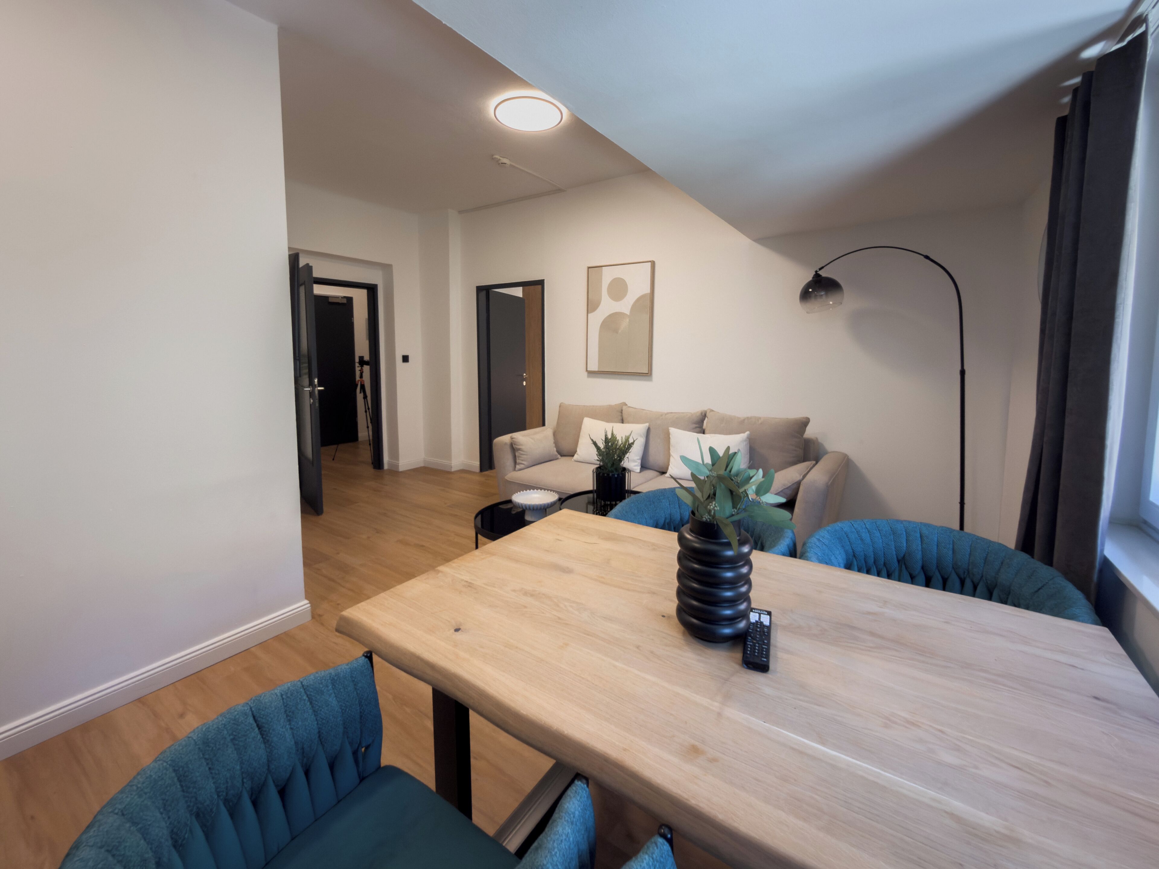 Un salon moderne avec une table à manger en bois, des chaises rembourrées bleues, un canapé, une lampe sur pied et une plante en pot.
