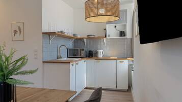 Une cuisine moderne avec des meubles blancs, un plan de travail en bois, un luminaire suspendu en rotin et une fougère en pot.