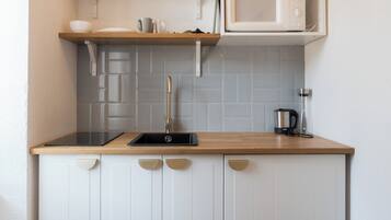 A kitchen with a wooden countertop, white cabinets, a sink, a microwave, and a kettle.