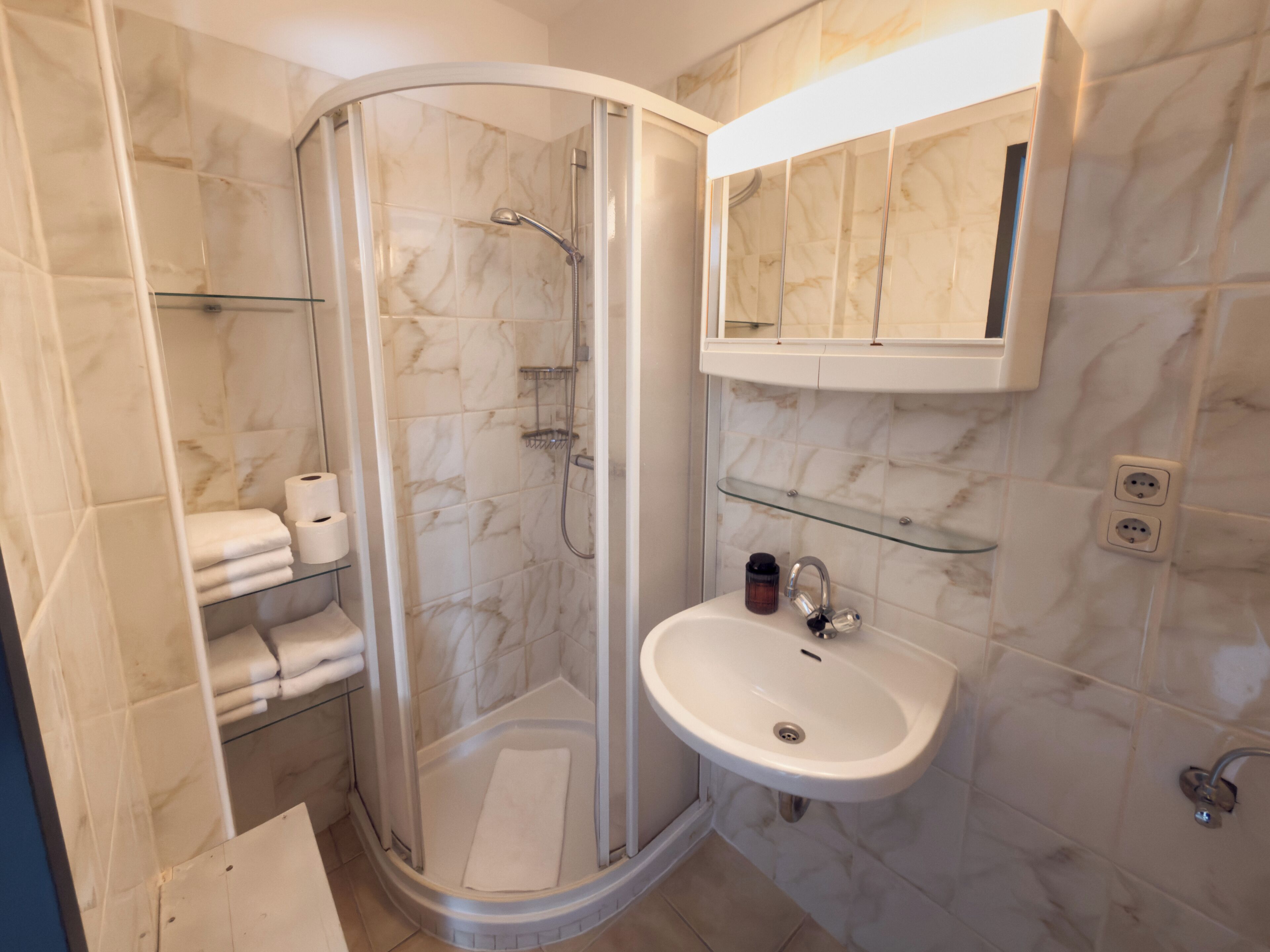 Une salle de bain moderne avec une douche à parois de verre, un lavabo blanc et un mur recouvert de carreaux de marbre.