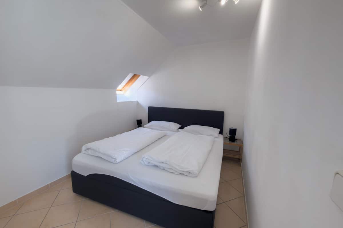 A bedroom with a bed, a nightstand, a lamp, and a skylight.