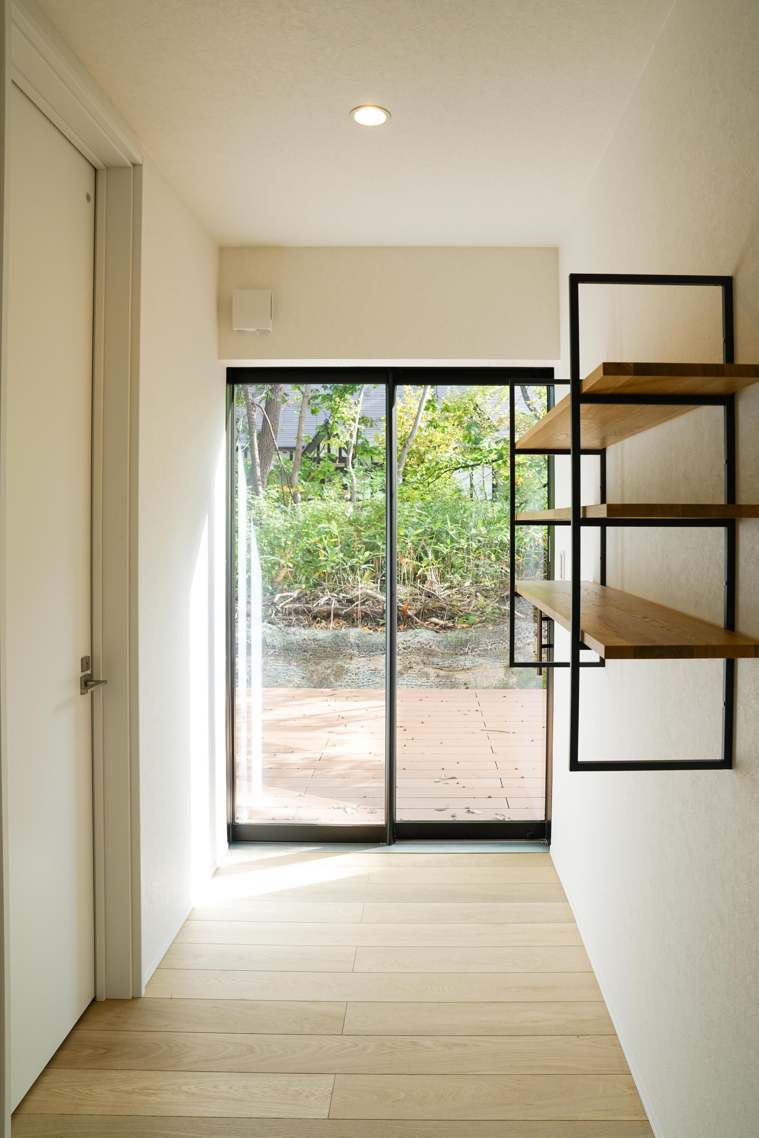 A room with a sliding glass door leading to an outdoor area, a wooden floor, and a wall-mounted shelf unit.