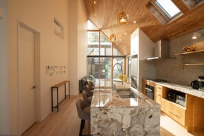A modern kitchen with a marble island, wooden ceiling, and large windows. - Echowoods.  Luxe. Fireplace. Onsen (Hakuba Village, Hokujo)