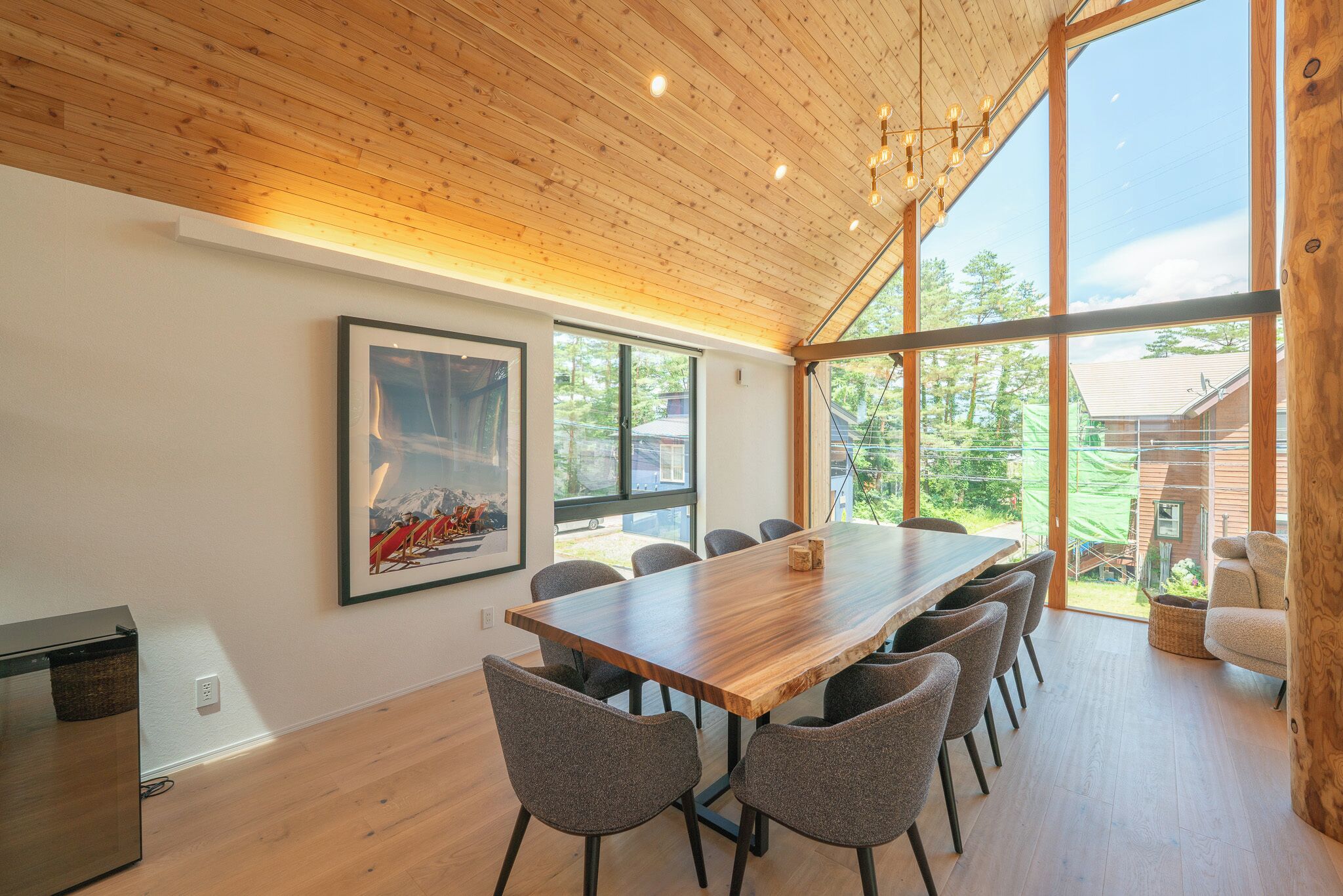 Un comedor moderno con una larga mesa de madera, múltiples sillas y un amplio ventanal con vistas al exterior.