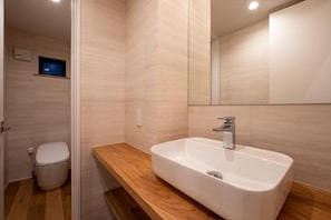 Une salle de bain avec un lavabo blanc, un plan de toilette en bois et un miroir au-dessus.