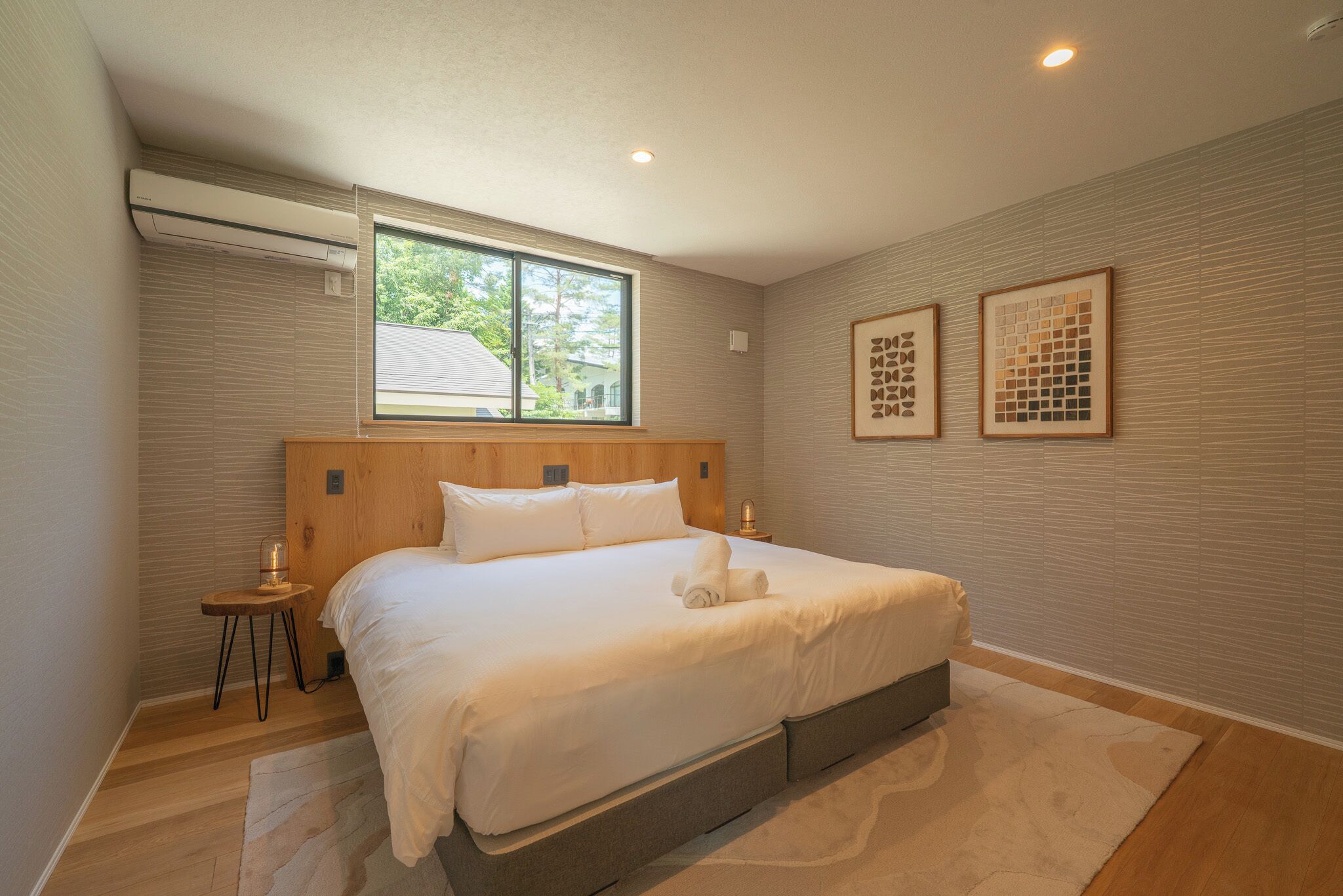 A bedroom with a large bed, a window, and two framed artworks on the wall.
