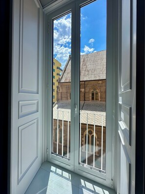 A room with a large window, white walls, and a view of a building with a tiled roof. - COMFORT AND ELEGANCE IN AN OASIS OF PEACE IN THE BEATING HEART OF NAPLES. (Napoli)