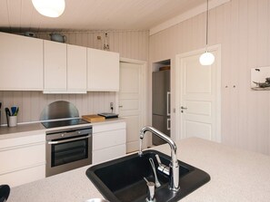 A kitchen with white cabinets, a stainless steel oven, a black sink with a modern faucet, and a hanging light fixture. - 4 Person Holiday Home in Hejls (Hejls)