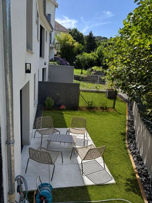 A patio with a table and chairs, a hose, and a grassy area.