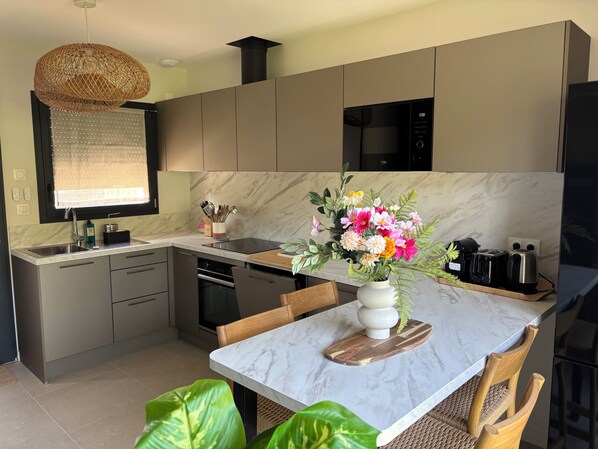 A modern kitchen with a marble countertop, a dining area with a white table, and a vase of flowers.