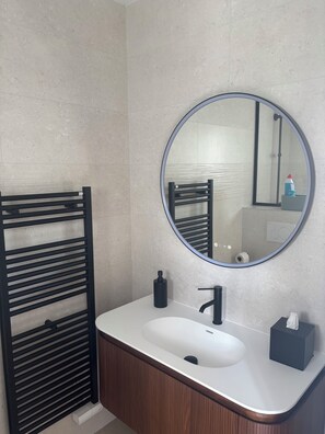 A bathroom with a round mirror, a black towel rack, a white sink, and a wooden cabinet.