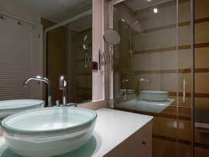 Un baño moderno con dos lavamanos de vidrio, un espejo y una ducha.