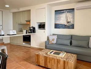 Un espacio habitable compacto con kitchenette, un sofá gris y una mesa de centro.