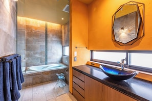 Ein modernes Badezimmer mit einer gläsernen Duschkabine, einer freistehenden Badewanne, einem Holzwaschtisch mit schwarzer Arbeitsplatte und einem großen Spiegel an der Wand.