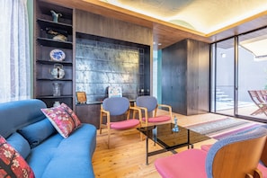 Ein modernes Wohnzimmer mit einem blauen Sofa, zwei Holzstühlen, einem Glastisch und einem großen Fenster mit Blick.