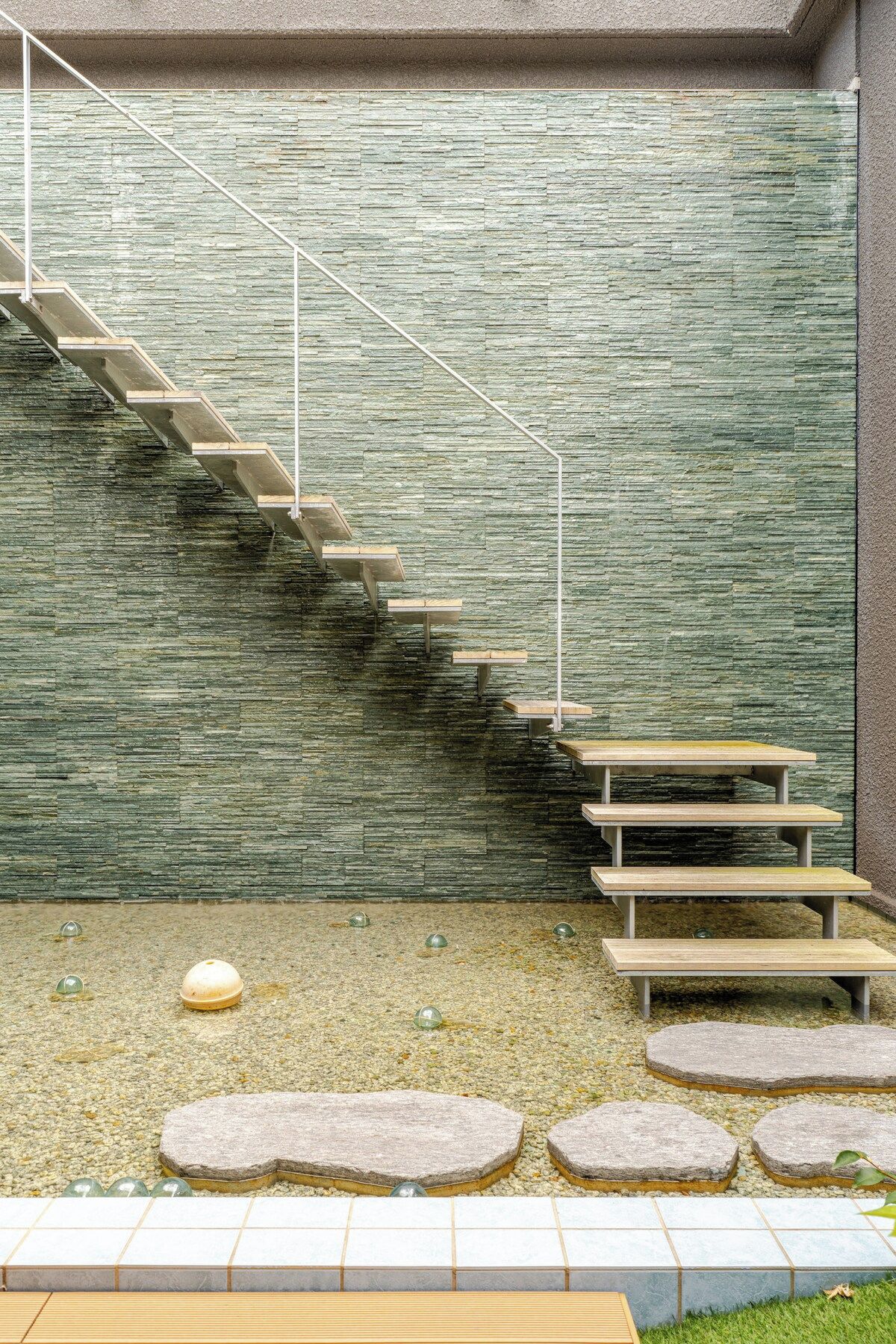 Eine Treppe mit einer Steinwand, Sitzgelegenheiten im Freien und einem Kiesgrund.