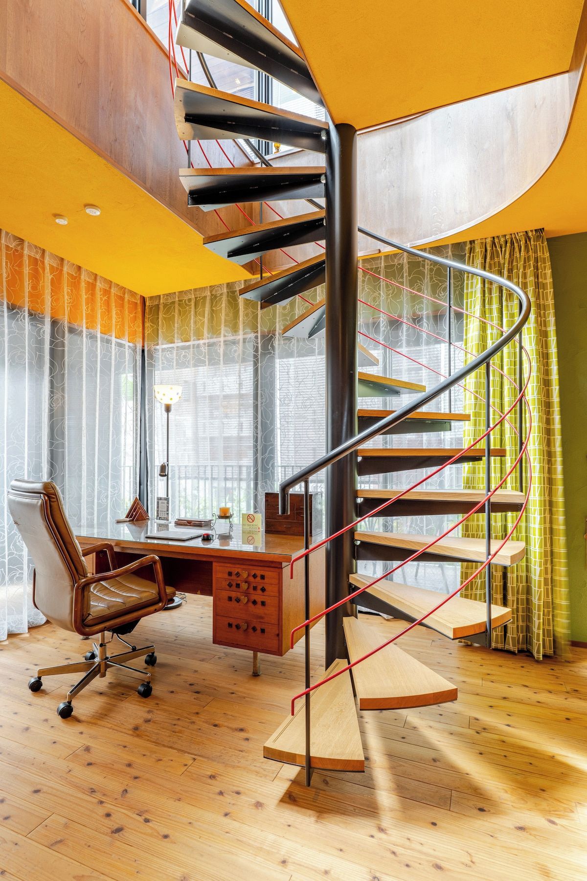 Un intérieur moderne avec un escalier en colimaçon, un bureau en bois, un fauteuil en cuir et de grandes fenêtres.