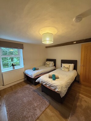 Quarto com duas camas, janela com vista, radiador e porta de madeira.