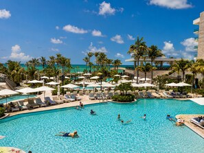 Zwembad van een resort met ligbedden, palmbomen en uitzicht op de oceaan.