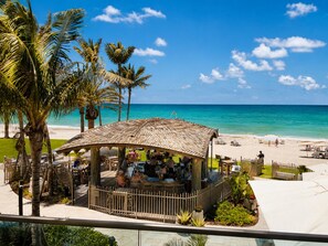Ein Restaurant direkt am Strand mit einem Reetdach, Sitzgelegenheiten im Freien und Meerblick.