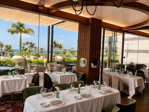 Ein Restaurant mit gedeckten Tischen, großen Fenstern mit Meerblick und modernem Interieur.