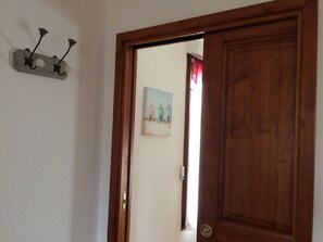 A wooden door with a brass doorknob, a wall-mounted light fixture with three bulbs, and a painting of houses in the background.