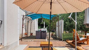 Une terrasse avec des chaises longues, une table et un espace barbecue.