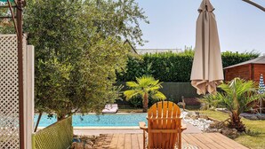 Une terrasse en bois avec une chaise et une table, une piscine et une clôture verte.