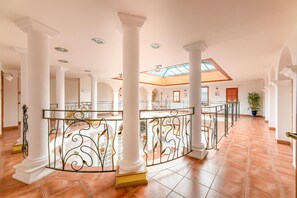 Een ruime binnenruimte met hoge plafonds, witte zuilen en een centraal balkon met versierde metalen hekwerk.