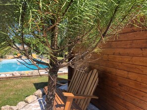A tree with a pool in the background, a wooden chair, and a wooden fence.