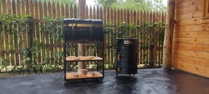 Un barbecue et une bouteille de propane se trouvent dans un espace extĂ©rieur agrĂ©mentĂ© dâune clĂŽture en bois et de verdure.