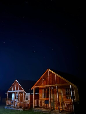 Dos cabañas de madera con techo a dos aguas y un porche, iluminadas en la noche.