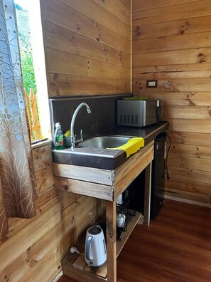 Una cocina compacta con un lavamanos, un microondas y una tetera.