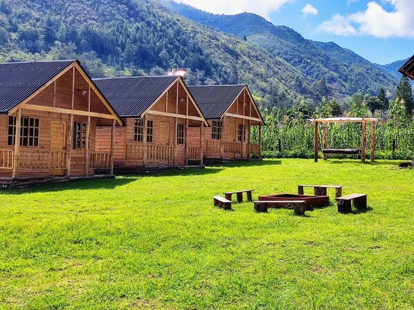 Un hilera de cabañas de madera con un patio cubierto de césped y un columpio.