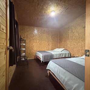Una habitación con dos camas, una pared de madera, un estante con toallas y una puerta con llave.