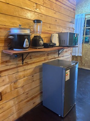 Una cocina con pared de madera, una encimera con una olla de cocción lenta, una licuadora, un microondas y un refrigerador.