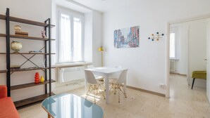 A modern living room with a white table, chairs, a glass coffee table, a bookshelf, and a painting on the wall. - Smart Lodging Rooftop Monti (Roma)