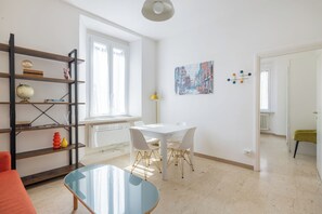 Een moderne woonkamer met een witte tafel, stoelen, een glazen salontafel, een boekenkast en een schilderij aan de muur.