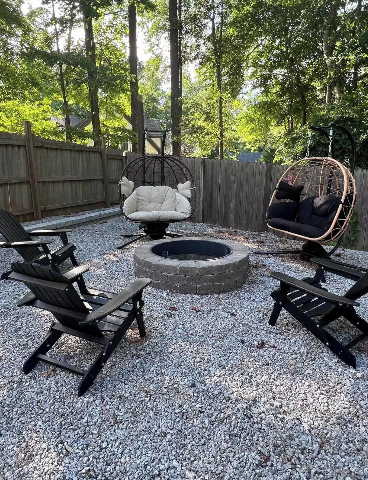Patio con un brasero, dos sillas Adirondack negras y una silla blanca acolchada.