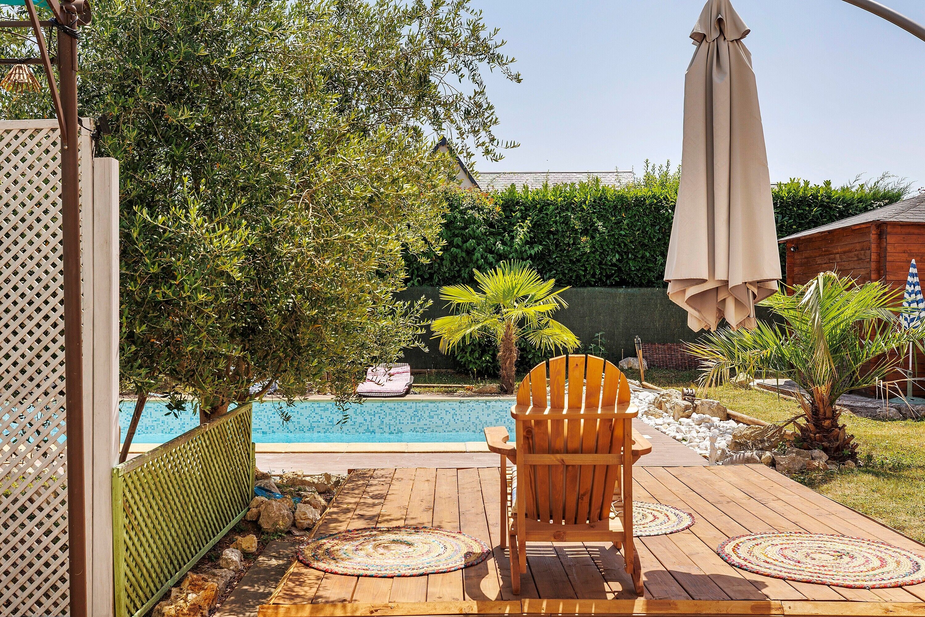A wooden deck with a chair and a table, a pool, and a green fence.