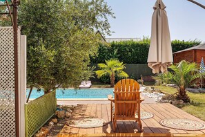 A wooden deck with a chair and a table, a pool, and a green fence. - Master Suite with Shared Pool (Saint-Cyr-sur-Loire)