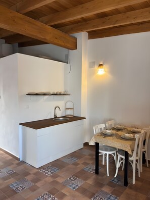 Une cuisine compacte avec un plafond en bois, un plan de travail blanc et un coin repas avec une table dressée pour quatre personnes.